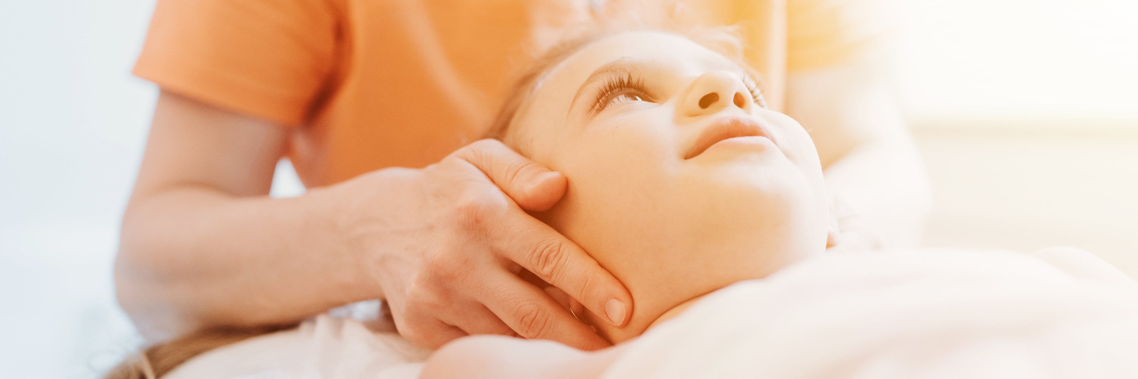 Person holding a child's head gently, with a blurred background
