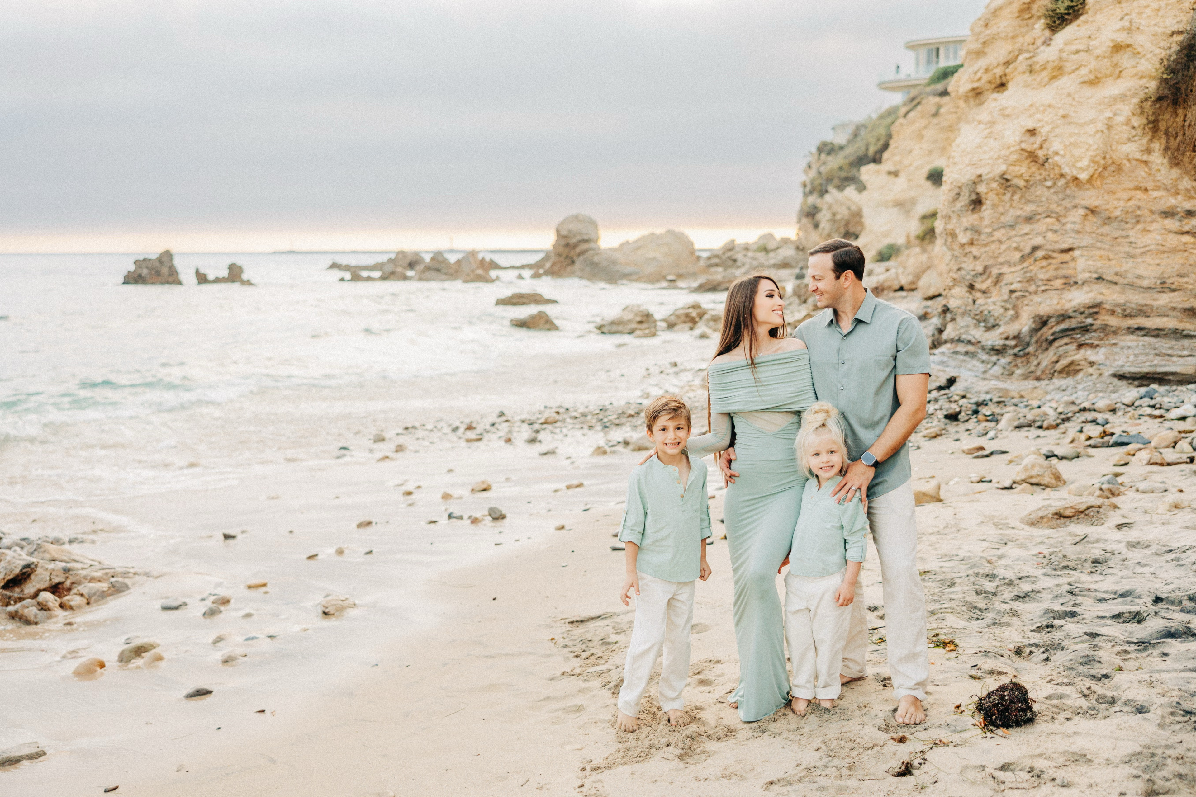 Family of four standing on a beach with ocean and cliffs in the background